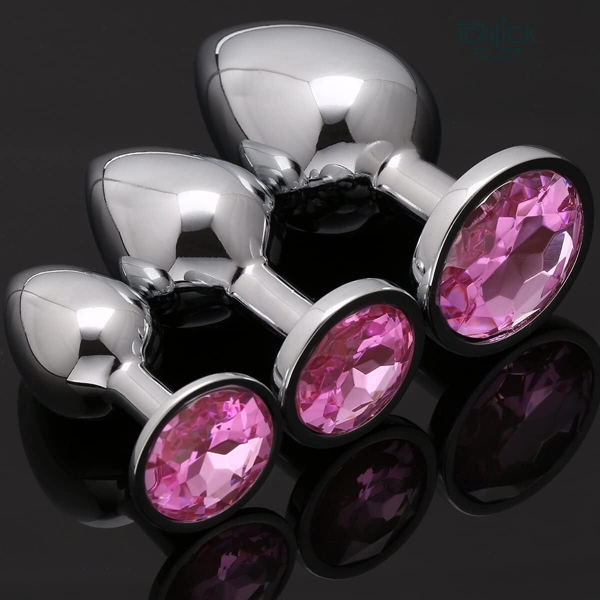 luxury-jewel-butt-plug-3-pieces-collection-toylick-2 A product photo of the three-piece Toylick jeweled butt plug set against a dark, reflective black background. The chrome finish and faceted pink jewels on the bases of the different-sized plugs are highlighted by the studio lighting.
